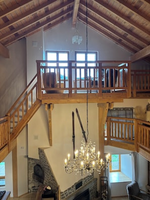 Um interior espaçoso com teto alto, vigas de madeira, lareira de pedra e um candelabro.