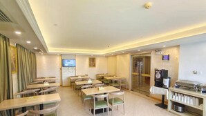 A hotel dining area with multiple tables and chairs, a television screen, and a refrigerator. - Vienna Hotel (Guangzhou)