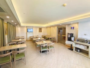 Une salle à manger d’hôtel avec plusieurs tables et chaises, un écran de télévision et un réfrigérateur.