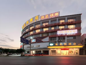 Un hôtel à plusieurs étages, doté d’une enseigne lumineuse, d’un restaurant visible au rez-de-chaussée et d’un parking rempli de voitures.