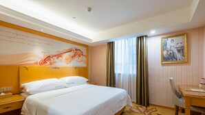 A hotel room with a large bed, a desk, a chair, a painting, and a decorative wall. - Vienna Hotel (Guangzhou)
