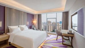 A hotel room with a large bed, a desk, a chair, and a view of the cityscape. - Lavande Hotel (Chengdu)
