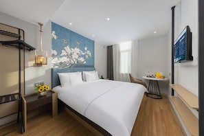 Ein modernes Hotelzimmer mit einem großen Bett, einem Gemälde an der Wand, einem Schreibtisch mit Stuhl und einem Fernseher.