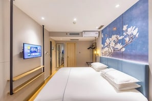 Ein Hotelzimmer mit einem Bett, einem an der Wand montierten Fernseher und einem Blumenbild.