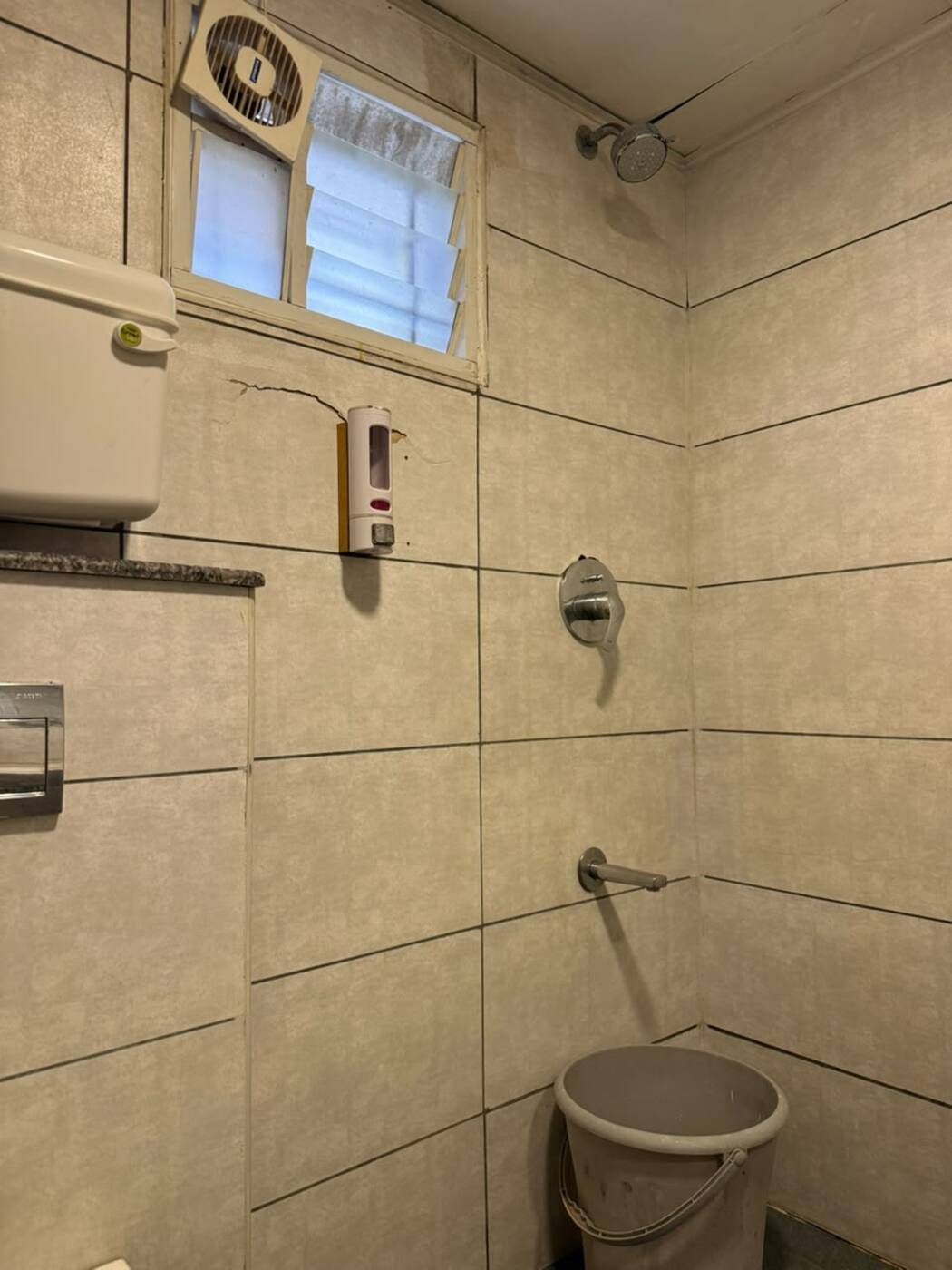 Un baño con ducha, inodoro, secamanos y ventana con persianas.