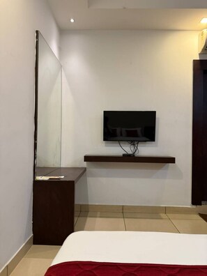 Un dormitorio moderno con una cama, un televisor en la pared, una mesita de noche y un espejo.