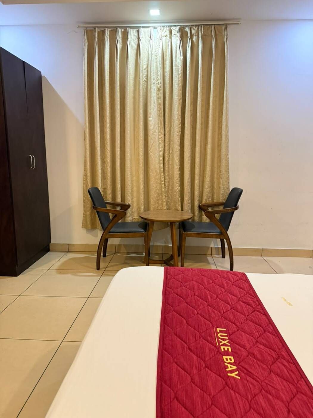 Una habitación de hotel con una cama, una mesita pequeña con dos sillas y un armario.
