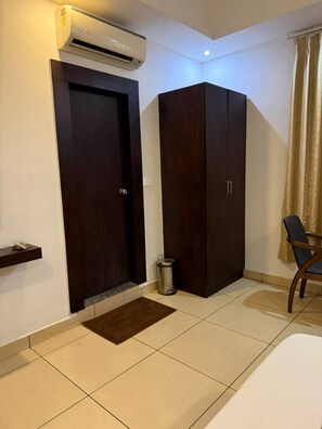 A room with a bed, a wardrobe, a trash bin, a chair, and an air conditioning unit. - LUXE BAY (Bengaluru)