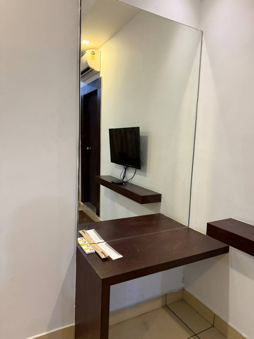 Una habitación con un espejo grande, un televisor de pantalla plana montado en la pared y un escritorio de madera con estante.