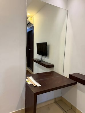 A room with a large mirror, a flat-screen TV mounted on a wall, and a wooden desk with a shelf. - LUXE BAY (Bengaluru)