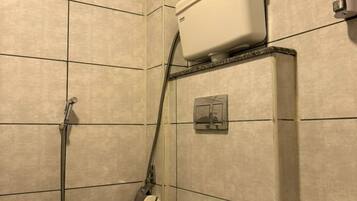 Un baño pequeño con azulejos, un inodoro, una manguera de ducha y un dispensador de papel higiénico.