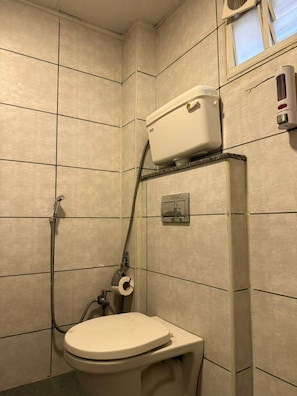 Ein kleines Badezimmer mit Fliesen, einer Toilette, einer Duschbrause und einem Toilettenpapierhalter.