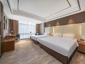 Une chambre d’hôtel avec deux lits, un bureau, une chaise et une vue sur la ville grâce à de grandes fenêtres.