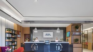 A hotel reception area with a modern design, featuring a reception desk, a large screen displaying the hotel name, and a seating area with a red chair and a purple sofa. - Campanile Hotel Shenzhen Honghuashan Metro Station (Shenzhen)