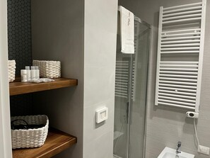 A modern bathroom with a glass shower enclosure, a white towel hanging on the door, and a shelf with toiletries. - Vrbo Property (Bari)