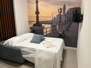 A hotel room with a bed, a view of a waterfront promenade, and a cityscape. - Vrbo Property (Bari)