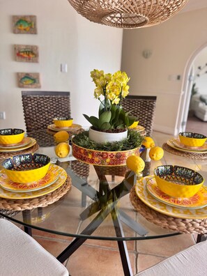 A glass-top table with yellow and patterned bowls and a central potted plant with yellow flowers.