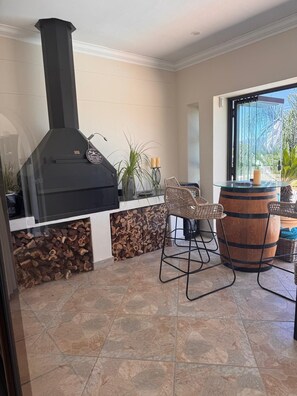 A patio area with a wood-burning stove, wicker chairs, a glass table, and a barrel.