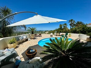 A rooftop pool area with a view of the city, outdoor seating, and a large umbrella.