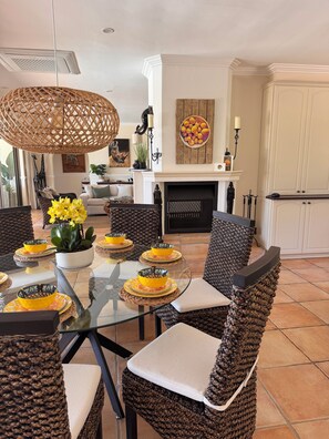 A dining area with a glass table, wicker chairs, yellow tableware, and a fireplace.