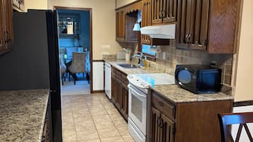 A kitchen with granite countertops, wooden cabinets, a refrigerator, an oven, a microwave, and a sink.