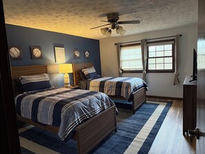 Een slaapkamer met twee bedden, een plafondventilator en een raam met gordijnen.