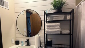 Ein Badezimmer mit einem weißen Waschbecken, einem Spiegel, einer Toilette, einem Handtuchhalter und einer Topfpflanze.
