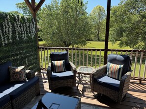 Una terraza con mobiliario de mimbre, incluyendo dos sillones y un sofá, con vista a un jardín césped y árboles.