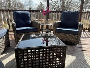 A deck with wicker furniture, including two chairs and a table, and a vase with flowers.
