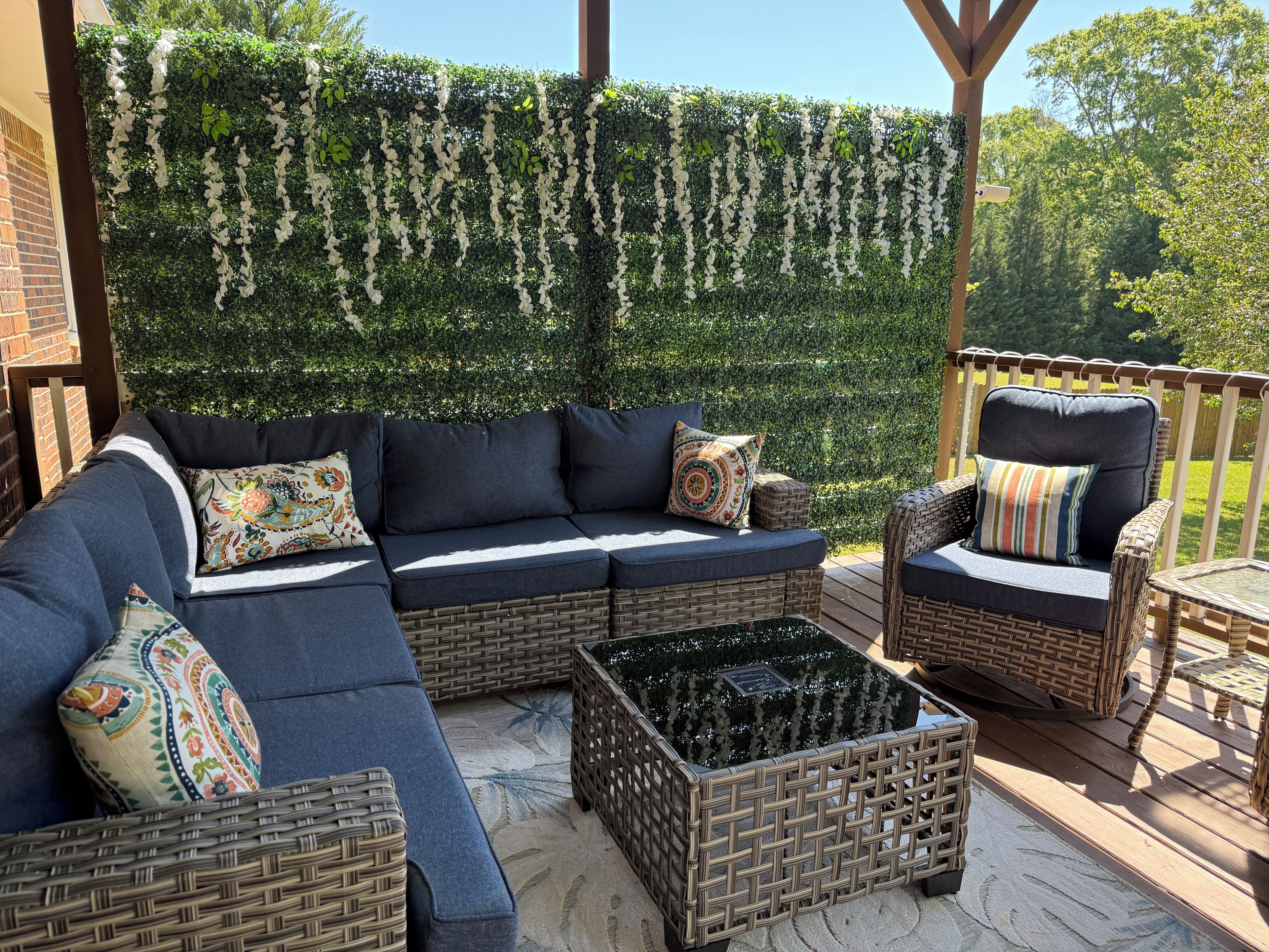 A covered outdoor seating area with a sectional sofa, two wicker chairs, and a small table.