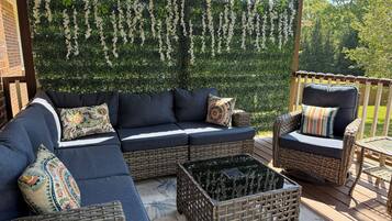 A covered outdoor seating area with a sectional sofa, two wicker chairs, and a small table.