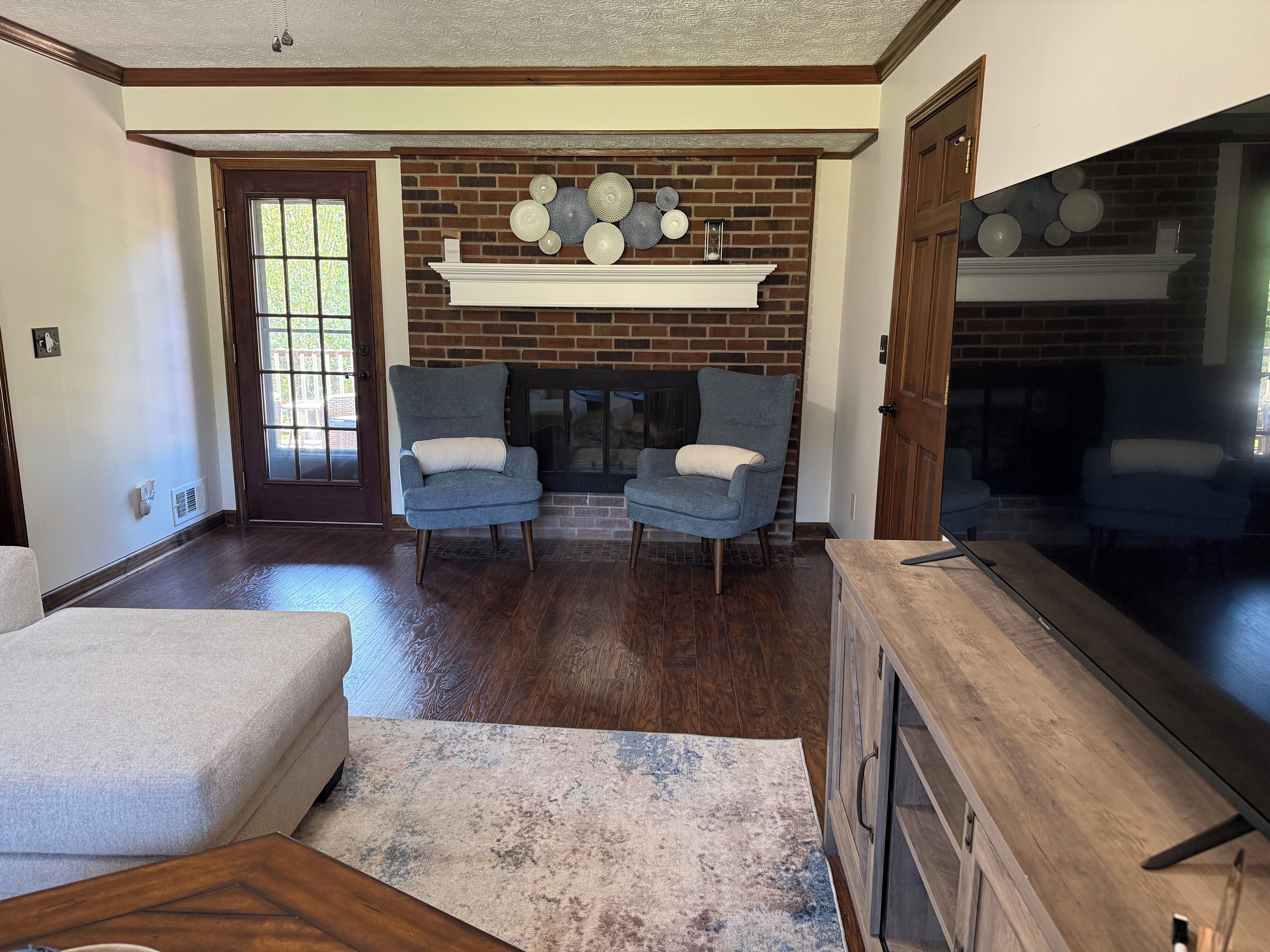 A living room with a fireplace, two armchairs, a sofa, and a television.