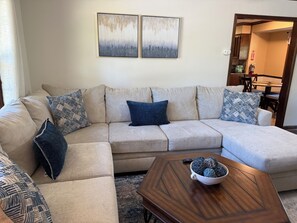 A living room with a beige sectional sofa, patterned throw pillows, a wooden coffee table, and abstract wall art.
