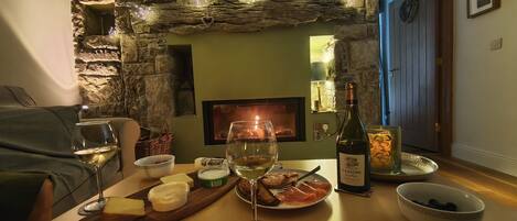 A cozy dining area with a stone wall, a fireplace, and a table set with food and drinks.