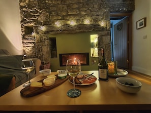 A cozy dining area with a stone wall, a fireplace, and a table set with food and drinks. - Historic Burren Cottage, King Suite, Private Patio & Wild Atalantic Way base (CE)