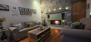 A cozy living room with a stone fireplace, a sofa, a coffee table, and a bookshelf. - Historic Burren Cottage, King Suite, Private Patio & Wild Atalantic Way base (CE)