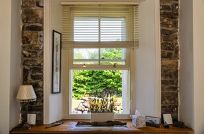 A room with a stone wall, a window with blinds, a framed picture, a lamp, and a small table with a vase and a tissue box. - Historic Burren Cottage, King Suite, Private Patio & Wild Atalantic Way base (CE)