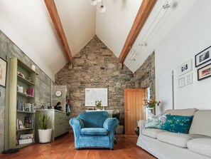 A cozy living room with a stone wall, a blue armchair, a white sofa, and a bookshelf. - Historic Burren Cottage, King Suite, Private Patio & Wild Atalantic Way base (CE)