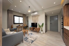 Ein modernes Wohnzimmer mit einem grauen Sofa, einem Esstisch mit Stühlen, einem Flachbildfernseher und einer Topfpflanze.
