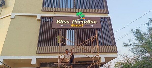 A sign for Bliss Paradise Resort with a tropical theme, including palm trees and a sun.