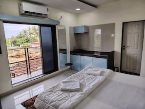 Ein Hotelzimmer mit Bett, einer kleinen Küchenzeile, einem Badezimmer und einem Balkon mit Blick ins Freie.