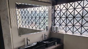 Une salle de bain dotée d’un comptoir en granit, d’un miroir, d’un lavabo et d’une fenêtre ornée d’un motif géométrique.