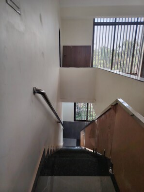 A staircase with a handrail, leading to a landing with a window overlooking greenery.