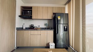 Una cocina compacta con microondas integrado, refrigerador de acero inoxidable y un pequeño cubo de basura.