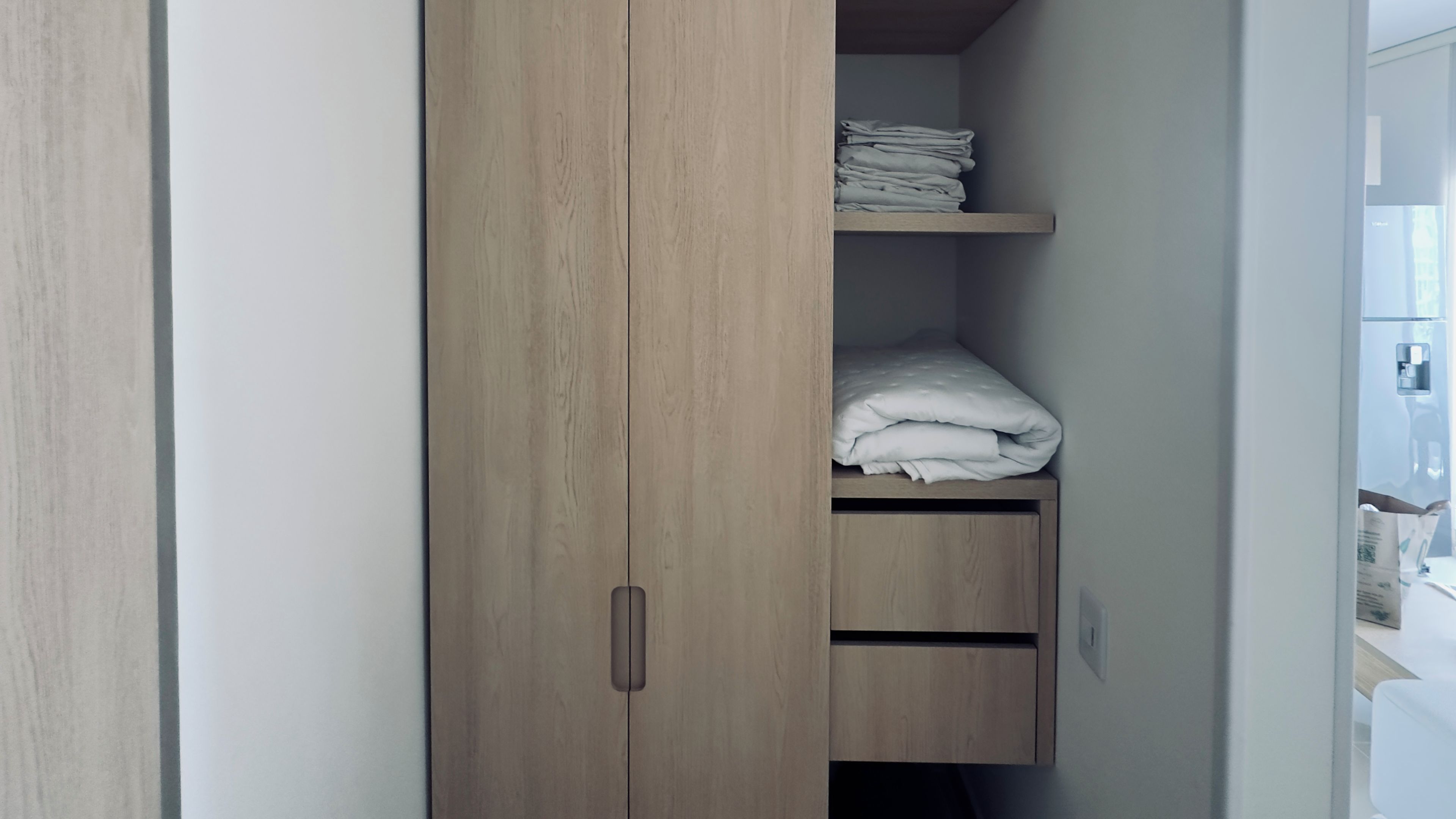 Un armario con acabado de madera, un estante con toallas dobladas y un cajón inferior.