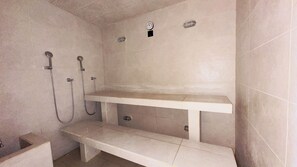 Un área de ducha con un banco, un estante en la pared y una ducha de mano.