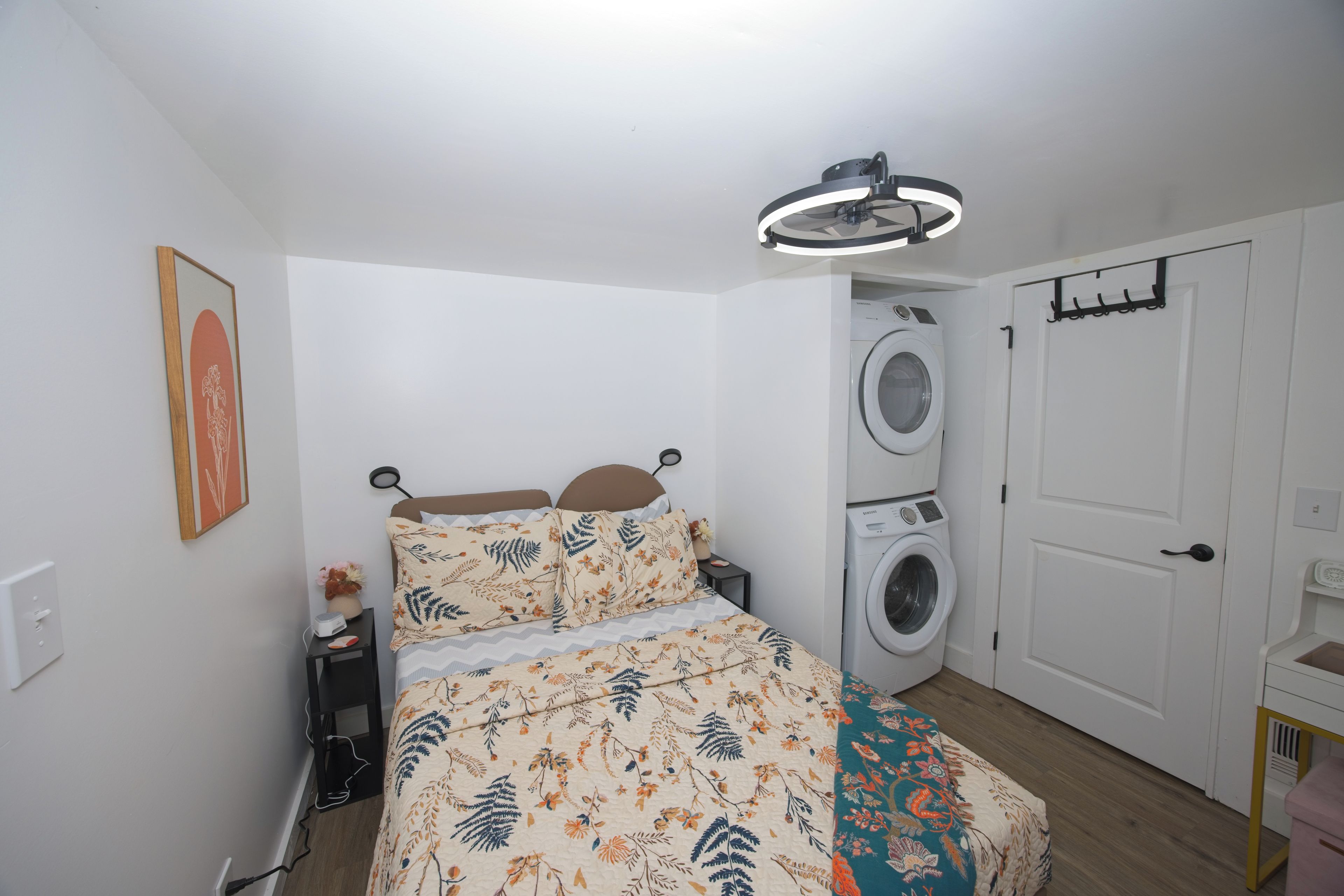 A bedroom with a bed, a washing machine, a door, and a wall-mounted light fixture.