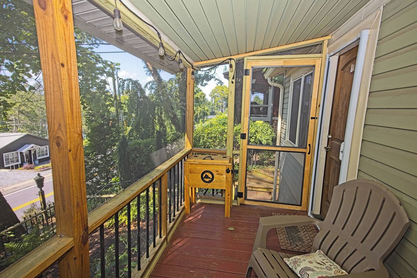 A wooden deck with a bench and a table, overlooking a street and greenery.