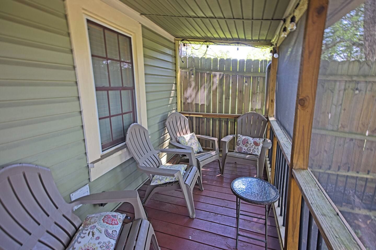 A porch with wooden railings, a table, and four chairs with floral cushions.