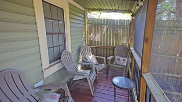 A porch with wooden railings, a table, and four chairs with floral cushions.